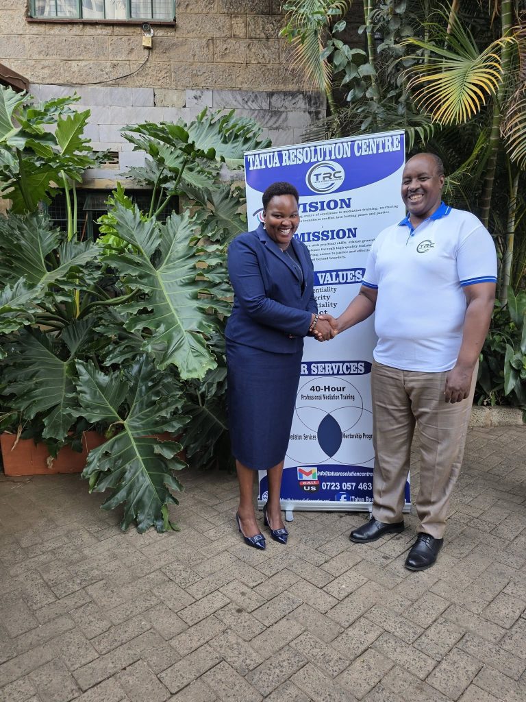 Two people greeting beside the Tatua Resolution Centre banner